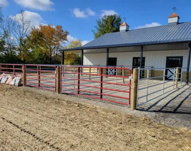 A horse stable with a red fence in front of it