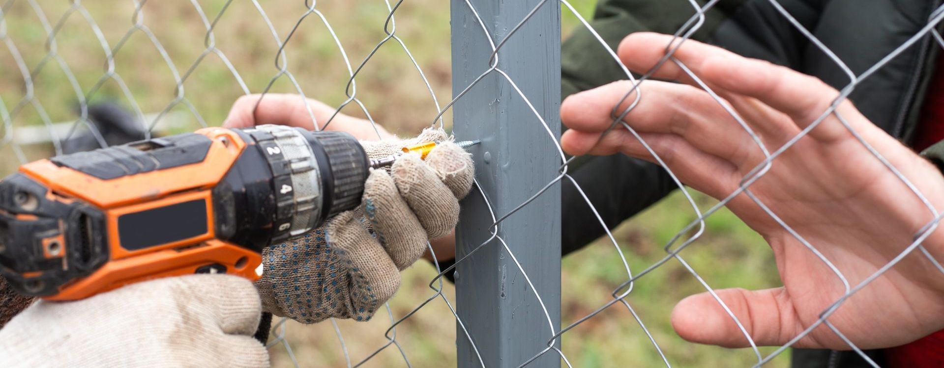 A man is using a drill to fix a chain link fence.