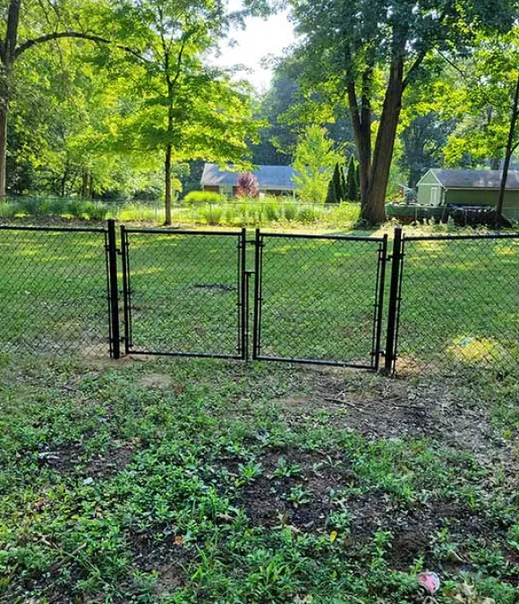 A chain link fence with a gate in the middle of a lush green field.