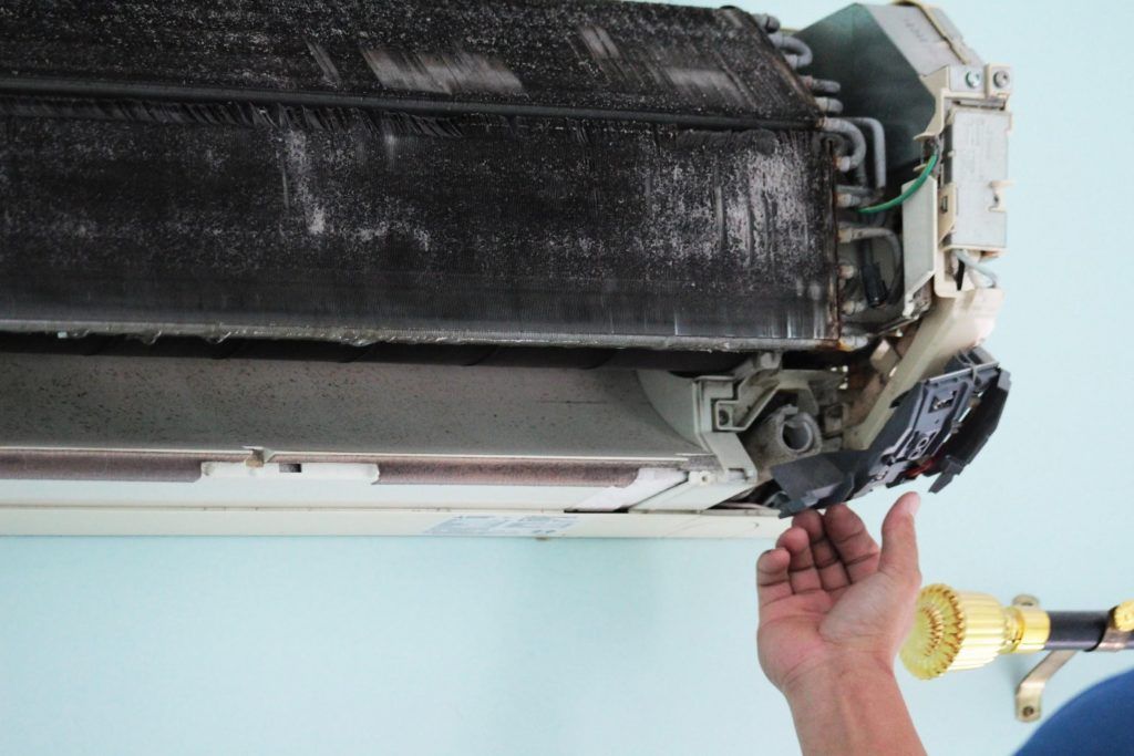 Hands in blue nitrile gloves holding a chrome P-trap pipe beneath a white bathroom sink.