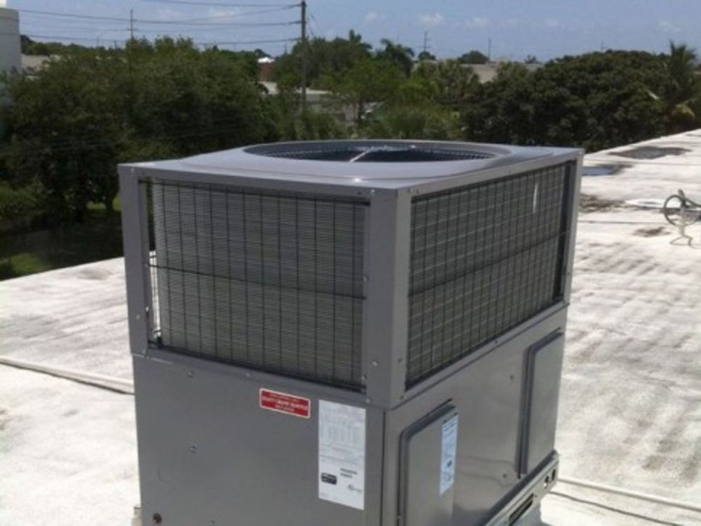 Gray rooftop HVAC unit on a white roof with trees and power lines in the background