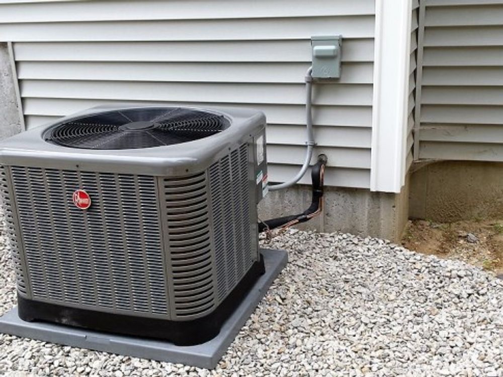 Outdoor air conditioning unit beside a house with white siding and gravel base