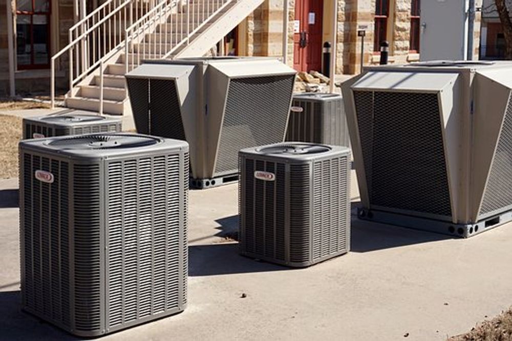 Outdoor HVAC units beside a building on a sunny pavement, including one small and several large metal units