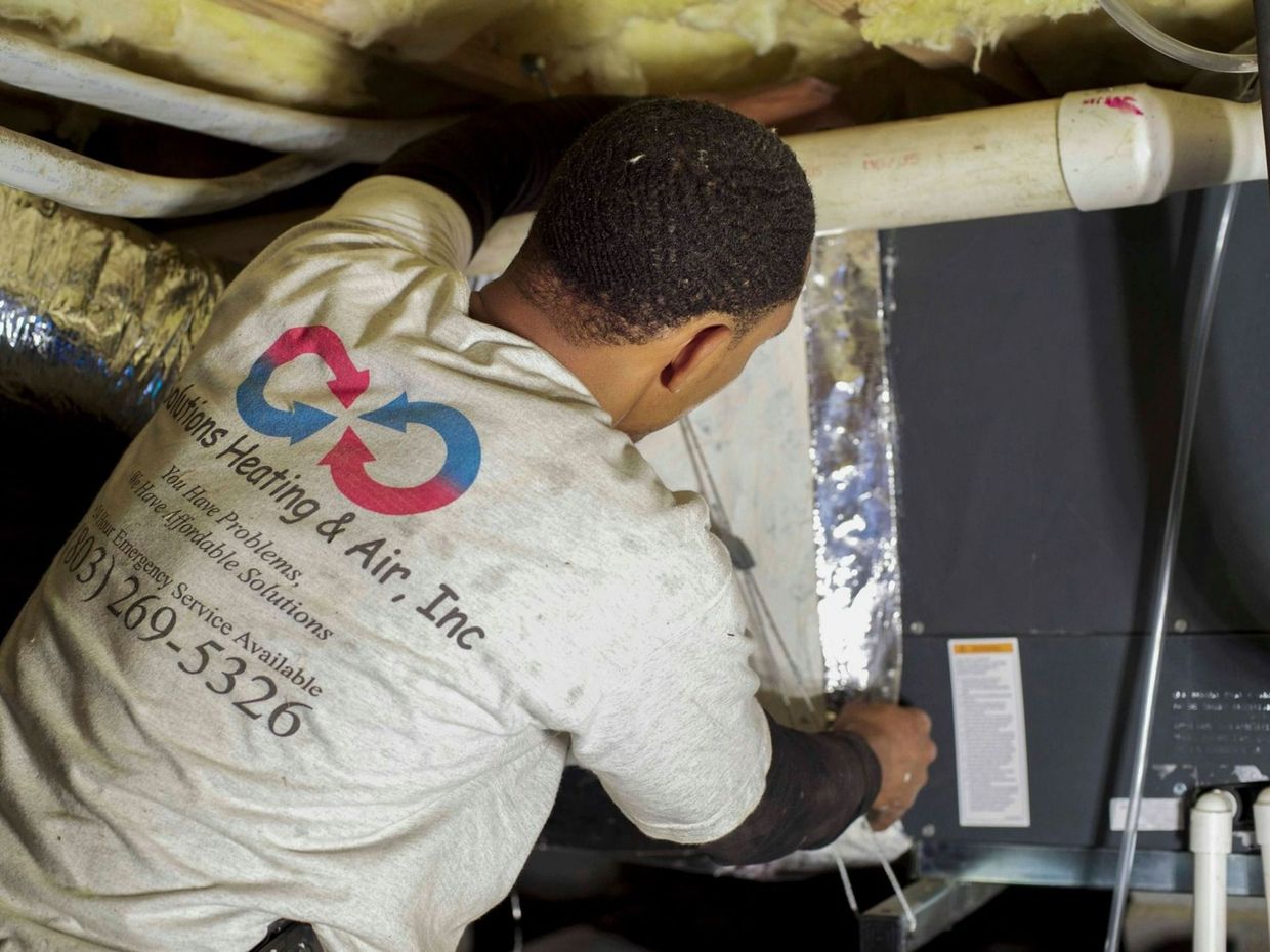 A technician in a blue shirt and protective gloves adjusts the controls of a piece of industrial machinery.