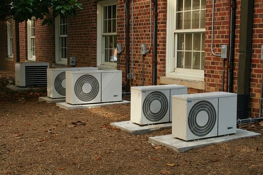 Three outdoor HVAC units beside a brick building with windows and a door.