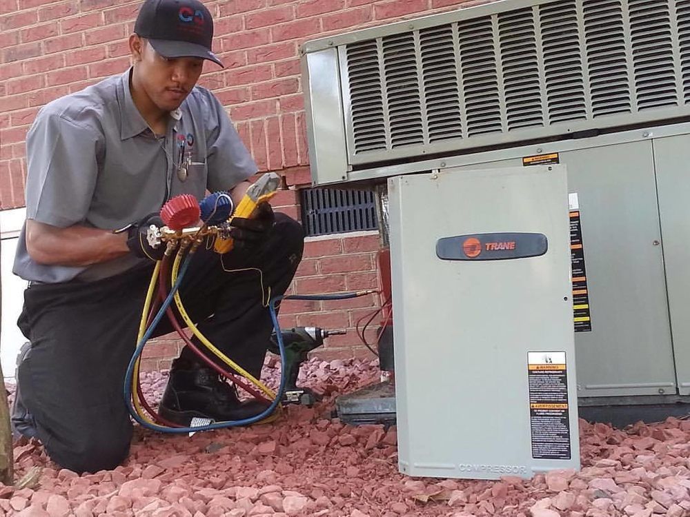 Technician kneeling beside outdoor HVAC unit, using gauges and hoses to inspect it.