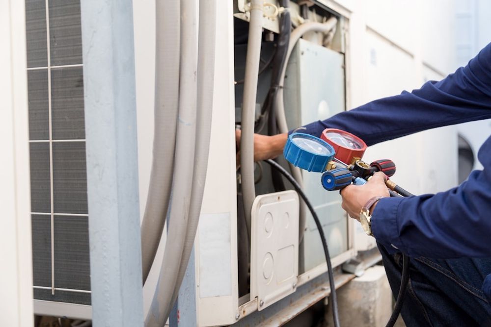 Hands in blue nitrile gloves holding a chrome P-trap pipe beneath a white bathroom sink.