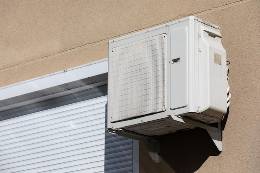 Wall-mounted air conditioning unit above a storefront window on a beige exterior wall
