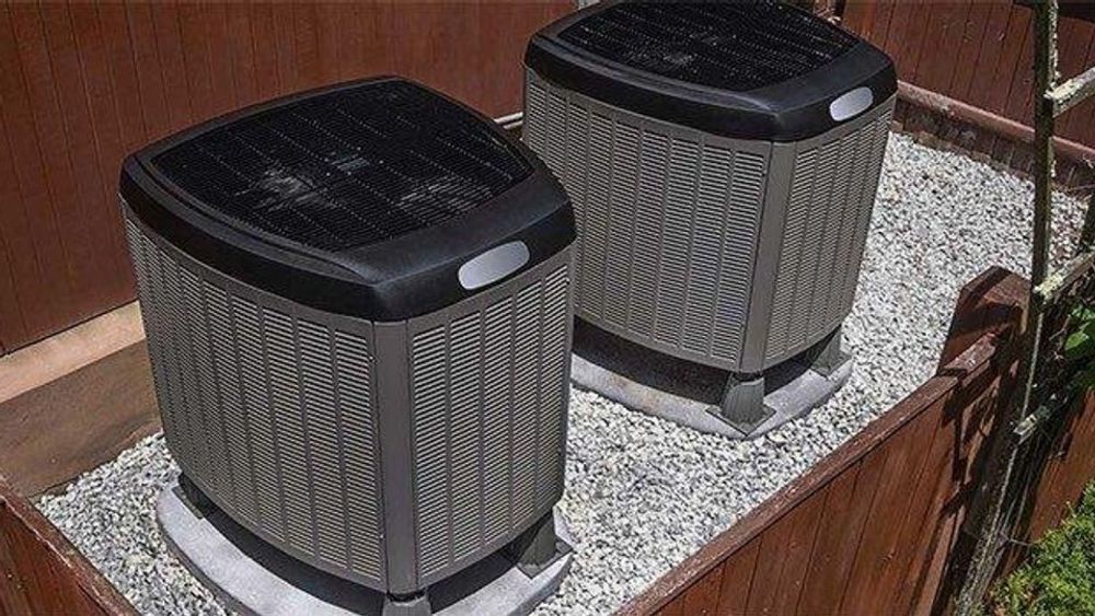 Two outdoor air conditioning units on a concrete pad beside a wall.
