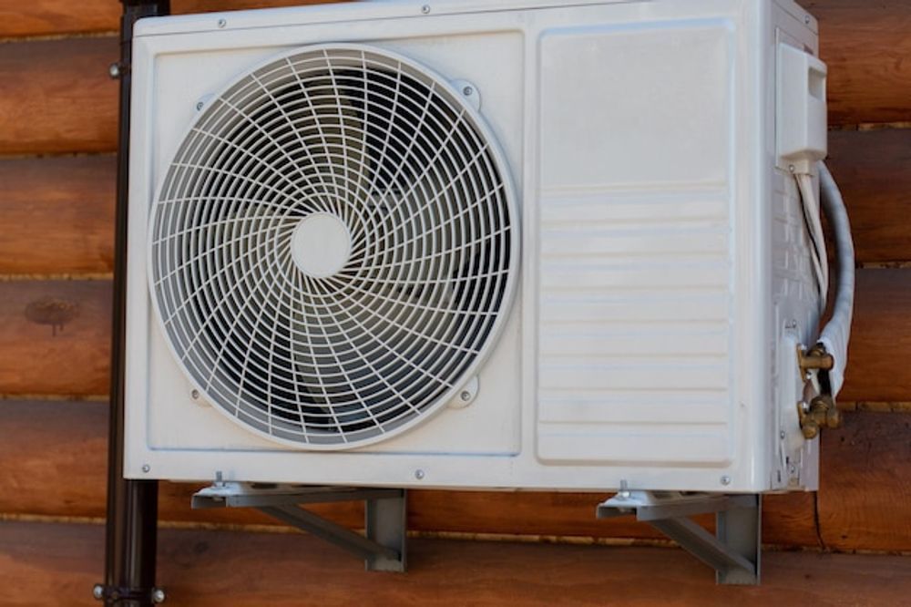 White outdoor air conditioner unit mounted on a wooden wall with a large front fan