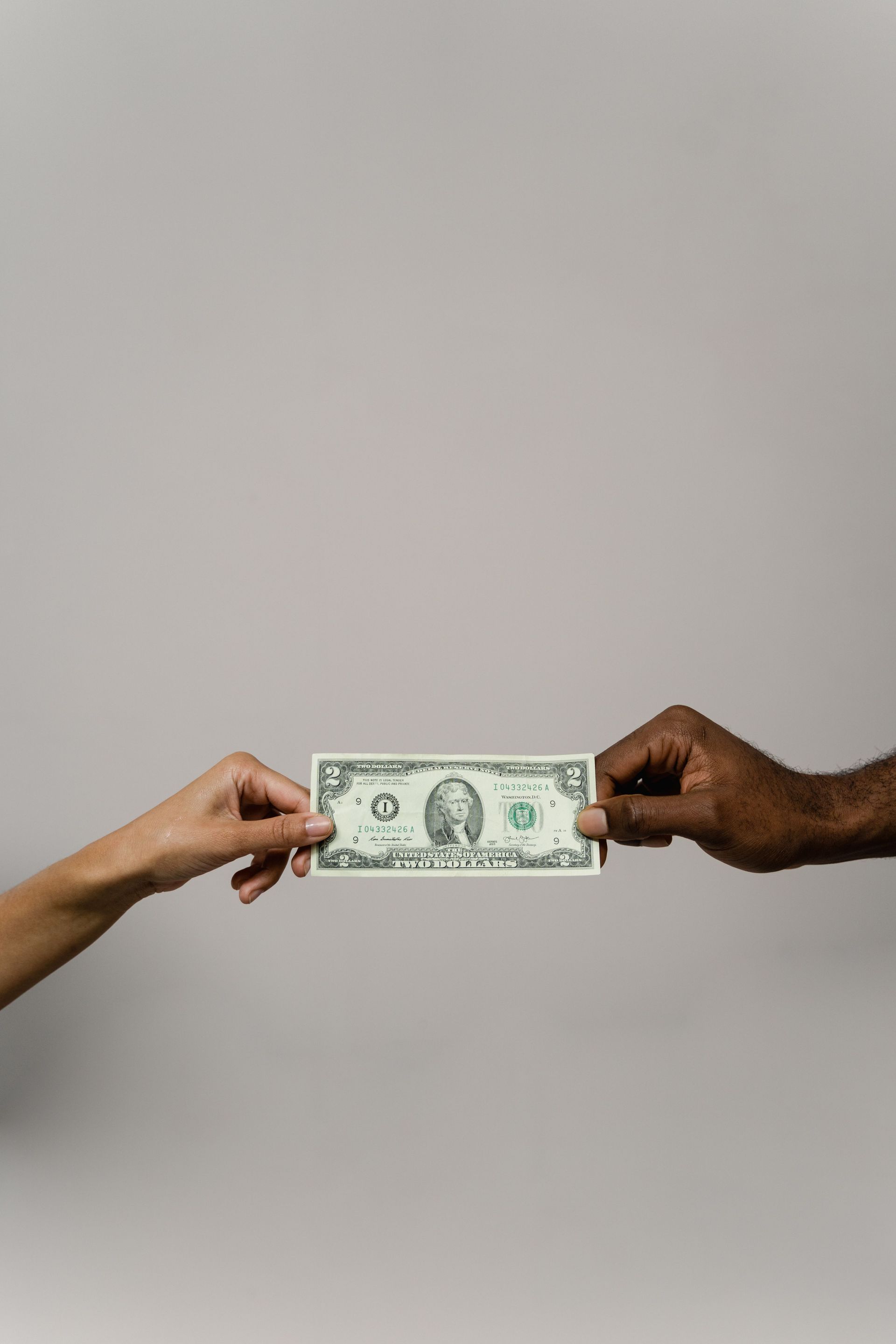 Two hands exchanging a one-dollar bill against a plain gray background
