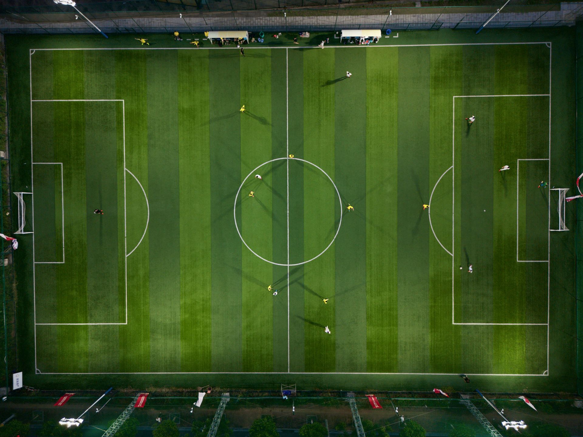 Aerial view of a rectangular green soccer field with white boundary lines and players scattered across the pitch.