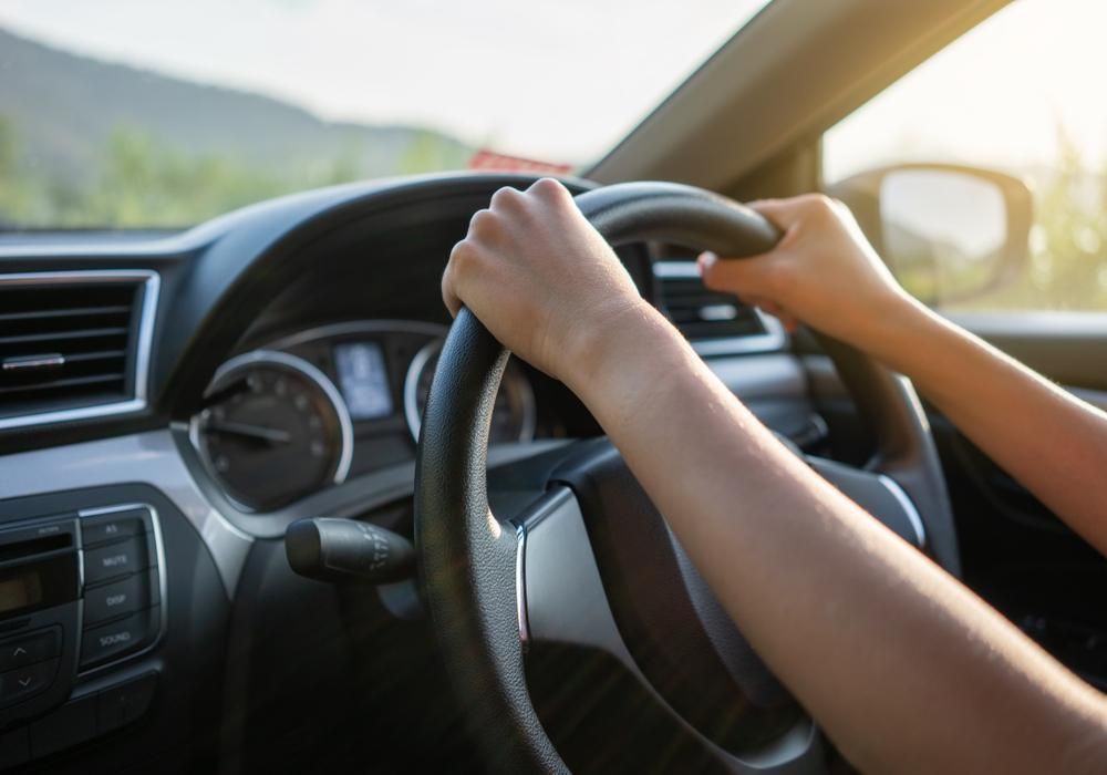 A Person Is Driving A Car With Their Hands On The Steering Wheel — Practic Automotive Services In Corrimal, NSW