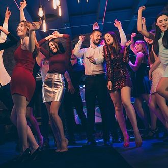 Un gruppo di amici ride e balla insieme in una discoteca scarsamente illuminata, dalle tonalità bluastre.
