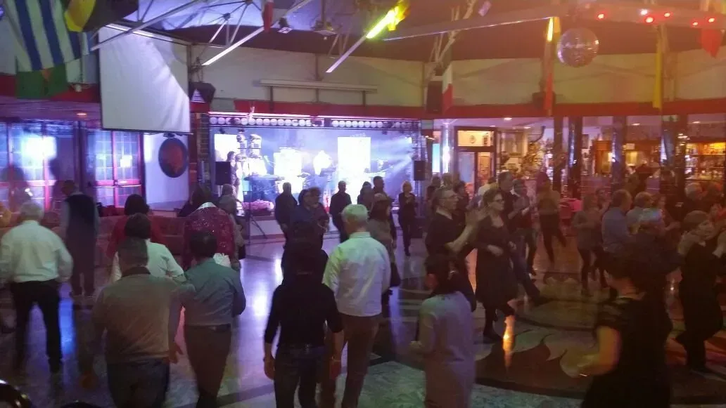 Un folto gruppo di persone balla su una pista da ballo in una sala scarsamente illuminata, con luci di scena e decorazioni sospese.