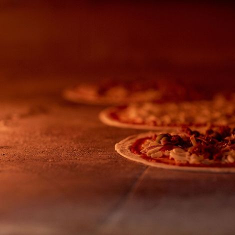 Diverse pizze cuociono su una superficie di pietra all'interno di un forno caldo e scarsamente illuminato.