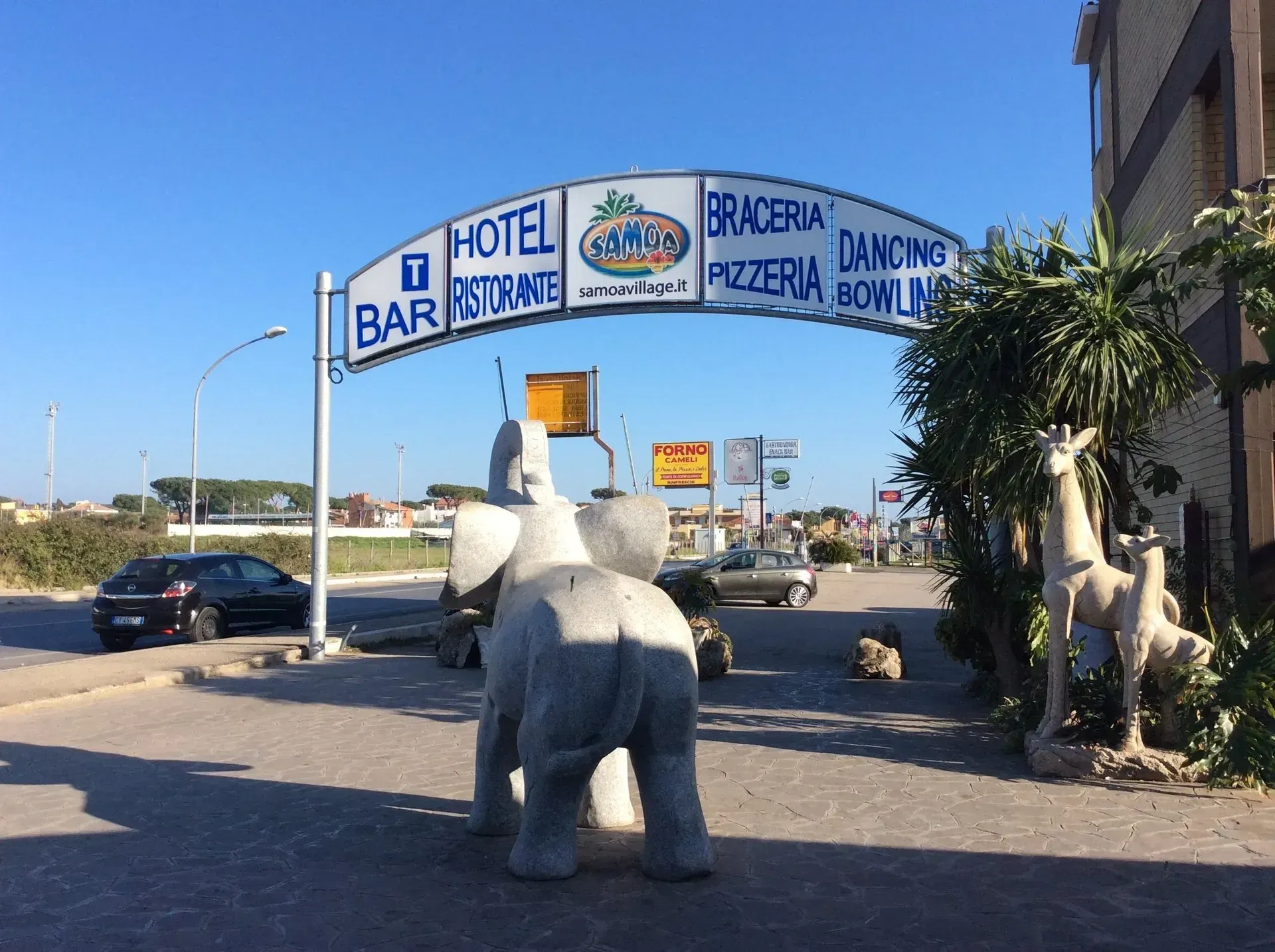 In una giornata di sole, una grande scultura di elefante in pietra si erge sotto l'insegna ad arco di un hotel, ristorante e bar.