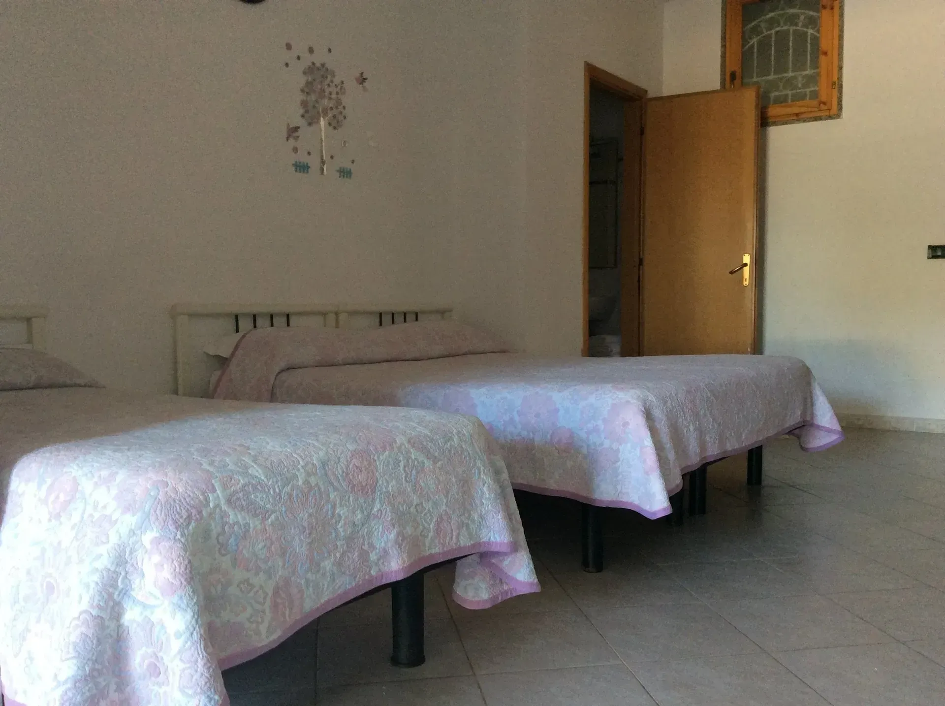 Una camera da letto con due letti singoli, biancheria da letto con motivi floreali bianchi e rosa, pareti chiare e una porta in legno.