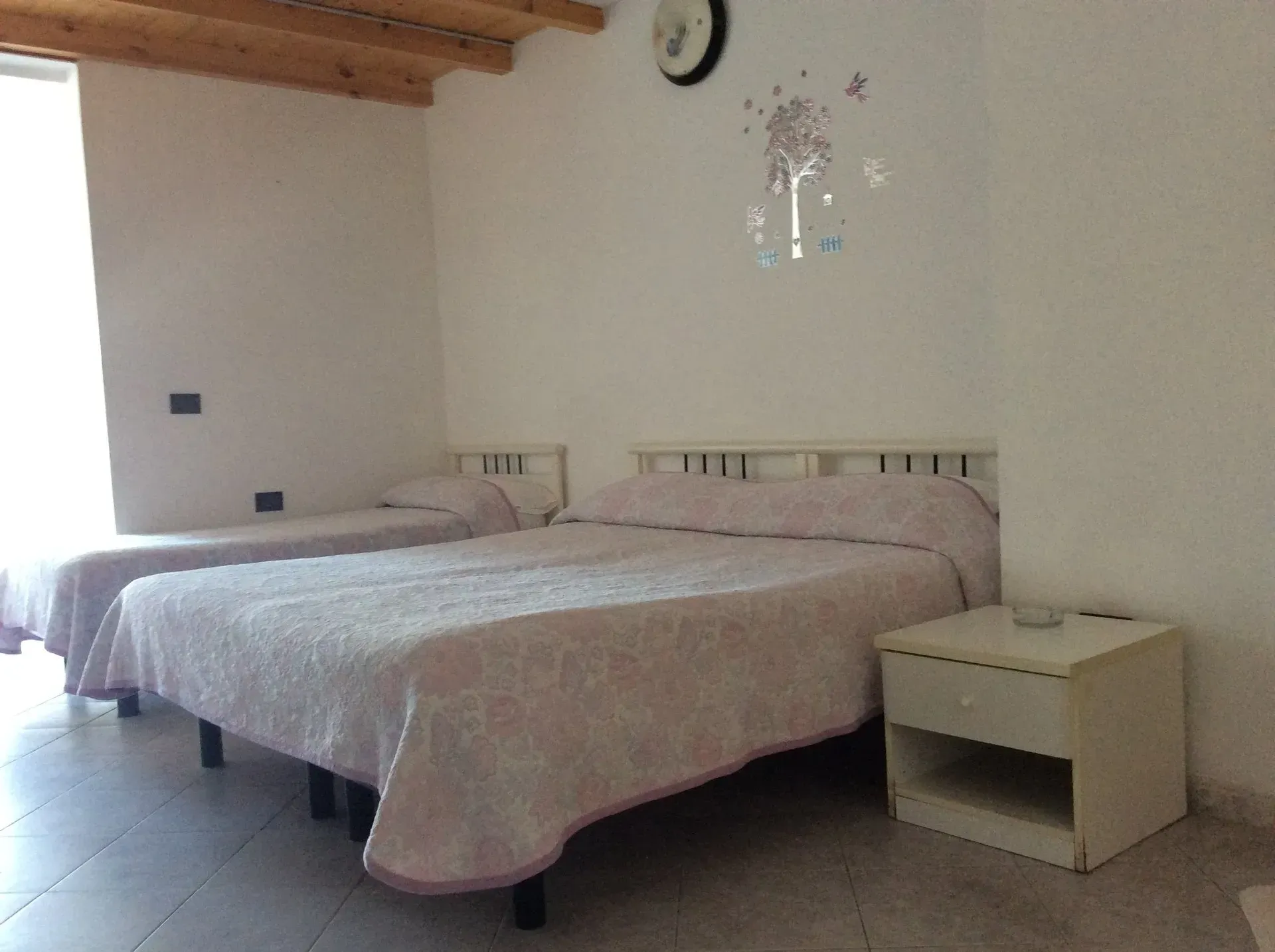 Una camera da letto con un letto matrimoniale e un letto singolo con copriletti a fantasia chiara, vicino a un comodino bianco.
