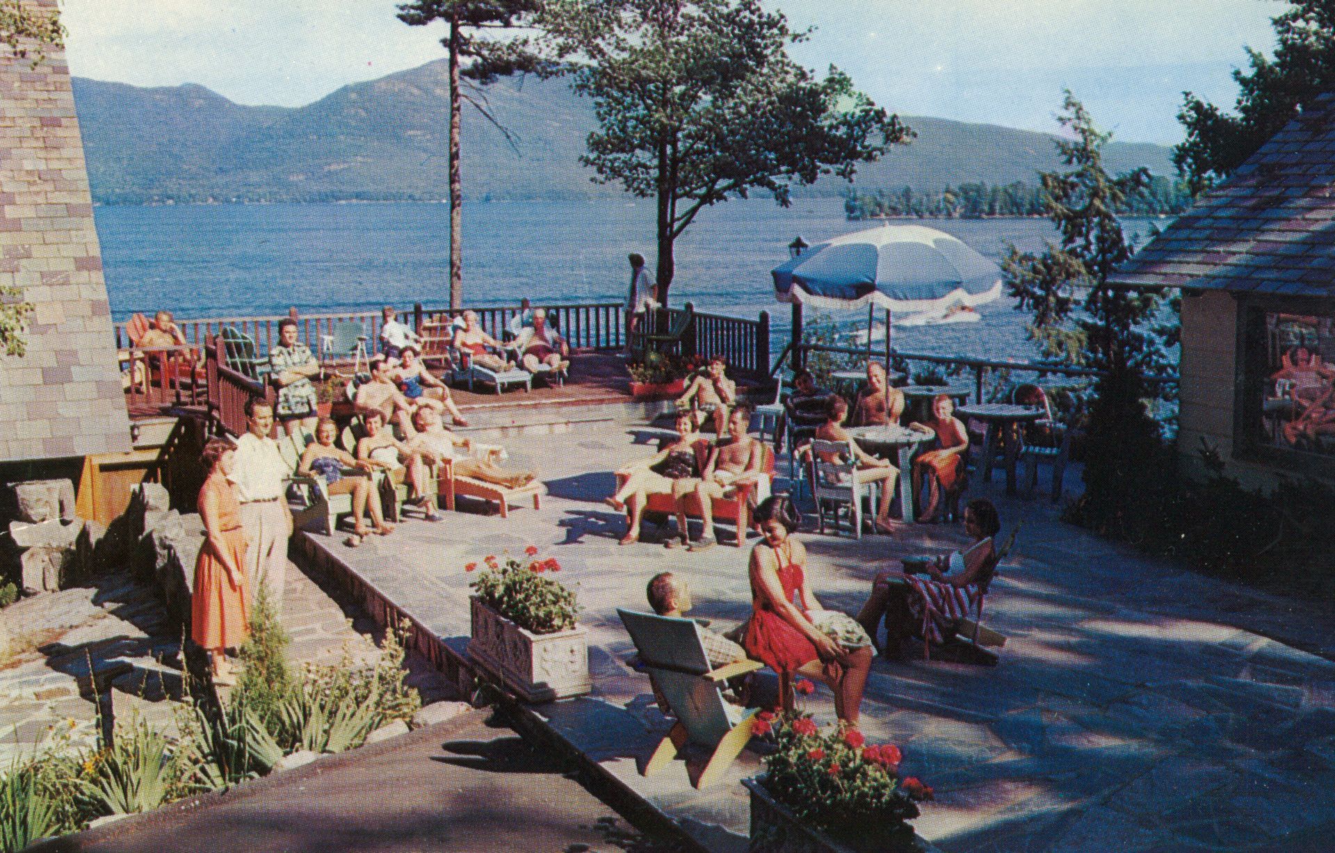 A group of people are sitting on a patio overlooking a lake