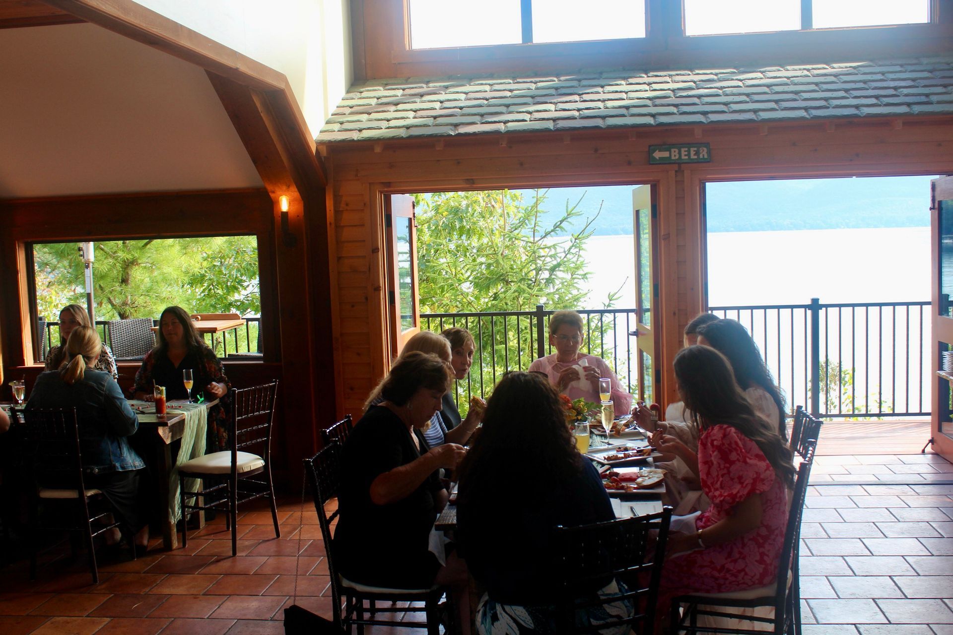 A group of people are sitting at tables in a room with a view of a lake.