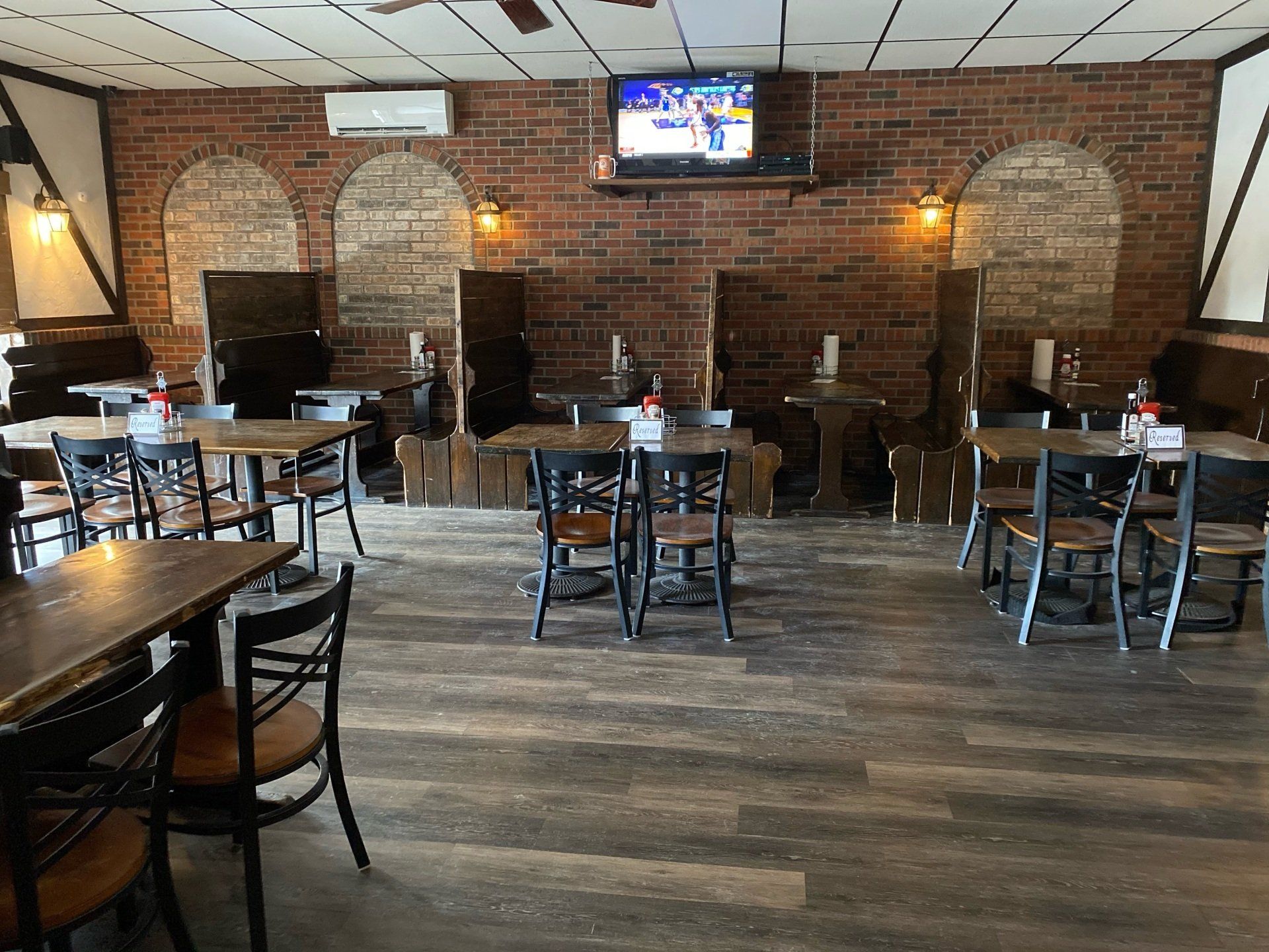 Interior of a restaurant with wooden tables and chairs, exposed brick wall, and a TV.