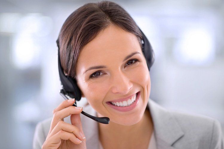 A smiling professional wearing a headset, hand near the microphone, against a blurred office background.