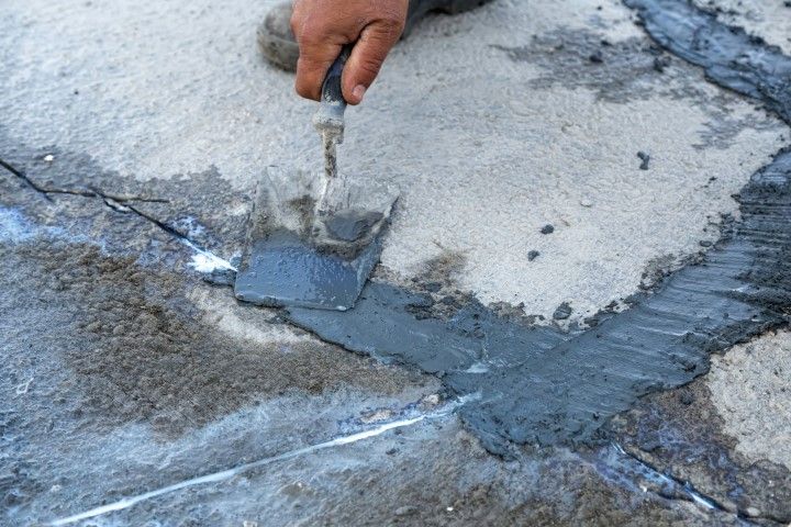 Person using a trowel to apply dark sealant to cracks in concrete.