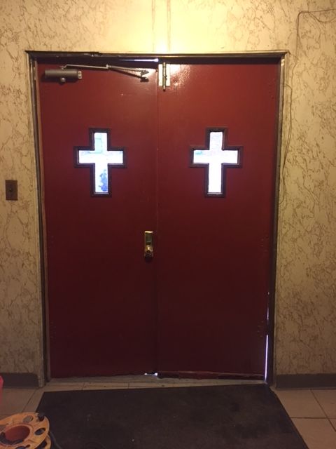 Interior of the old church double doors showing a single door closer, surface bolt, and daylight gap at the bottom edge