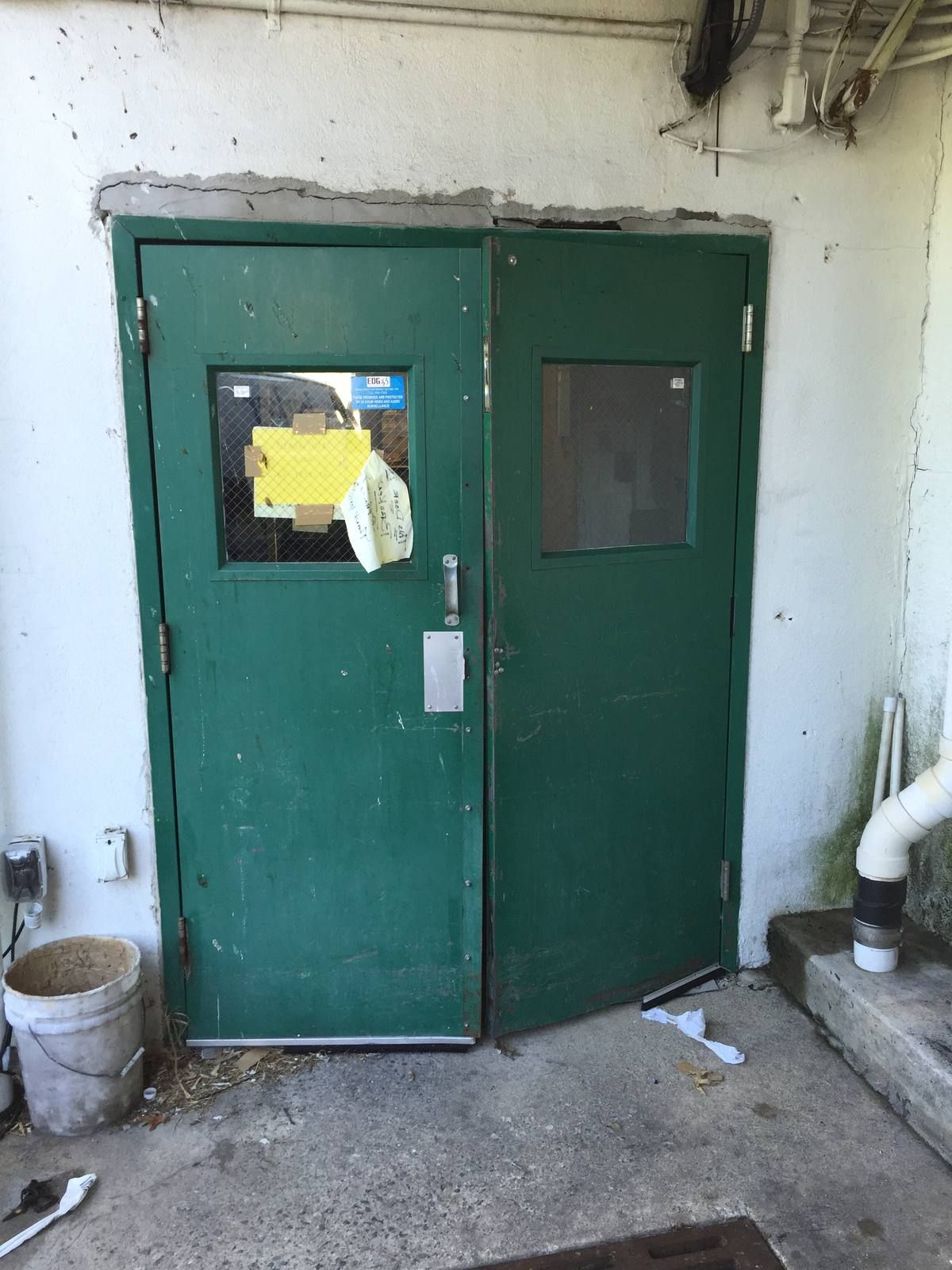 Old dented green steel double doors at a supermarket service entrance in Glen Rock, NJ, before replacement