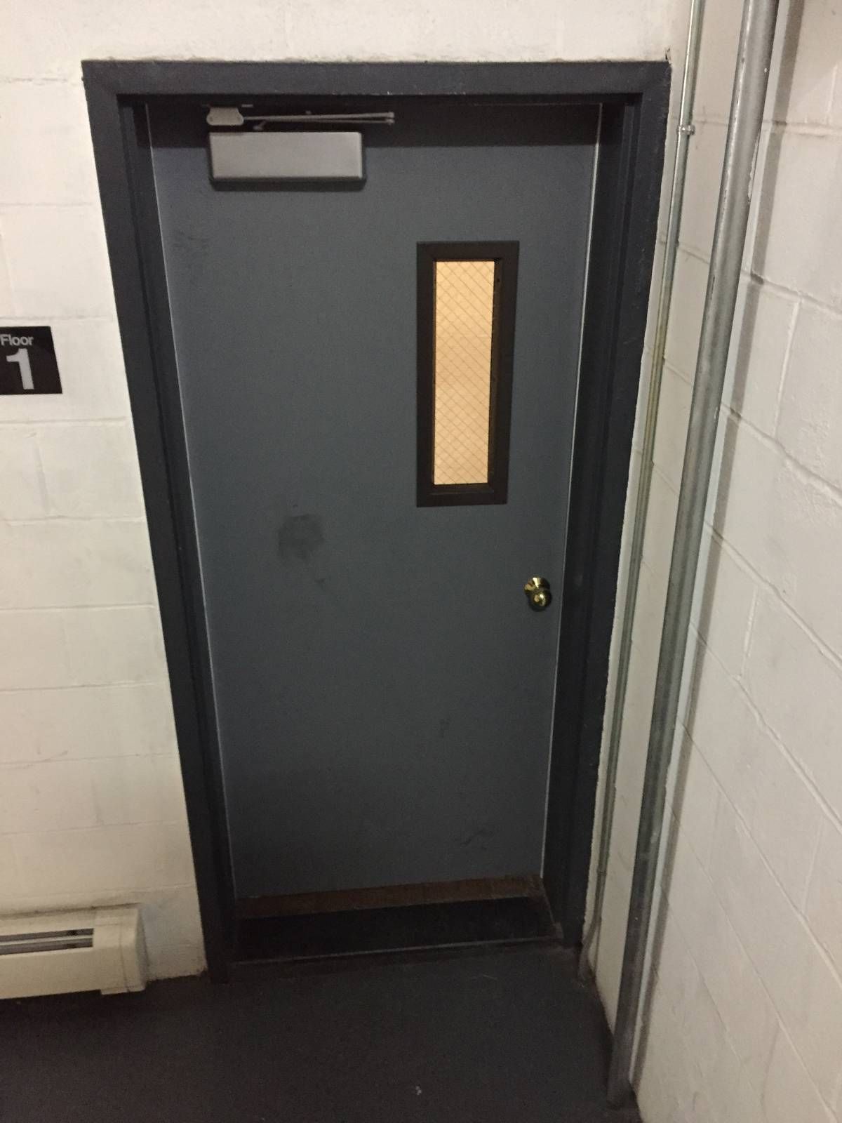 Hollow metal stairwell door with surface-mounted closer and wire-glass vision lite in a Manhattan apartment building