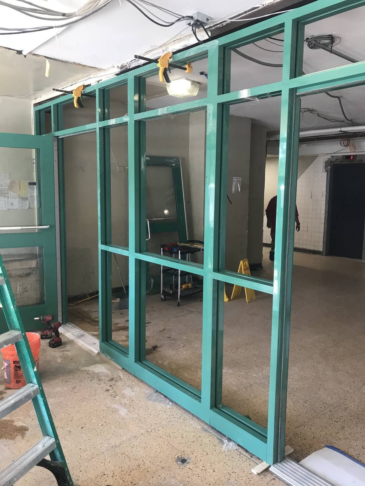 Aluminum storefront vestibule framing being set and clamped during installation in a Newark NJ apartment building lobby