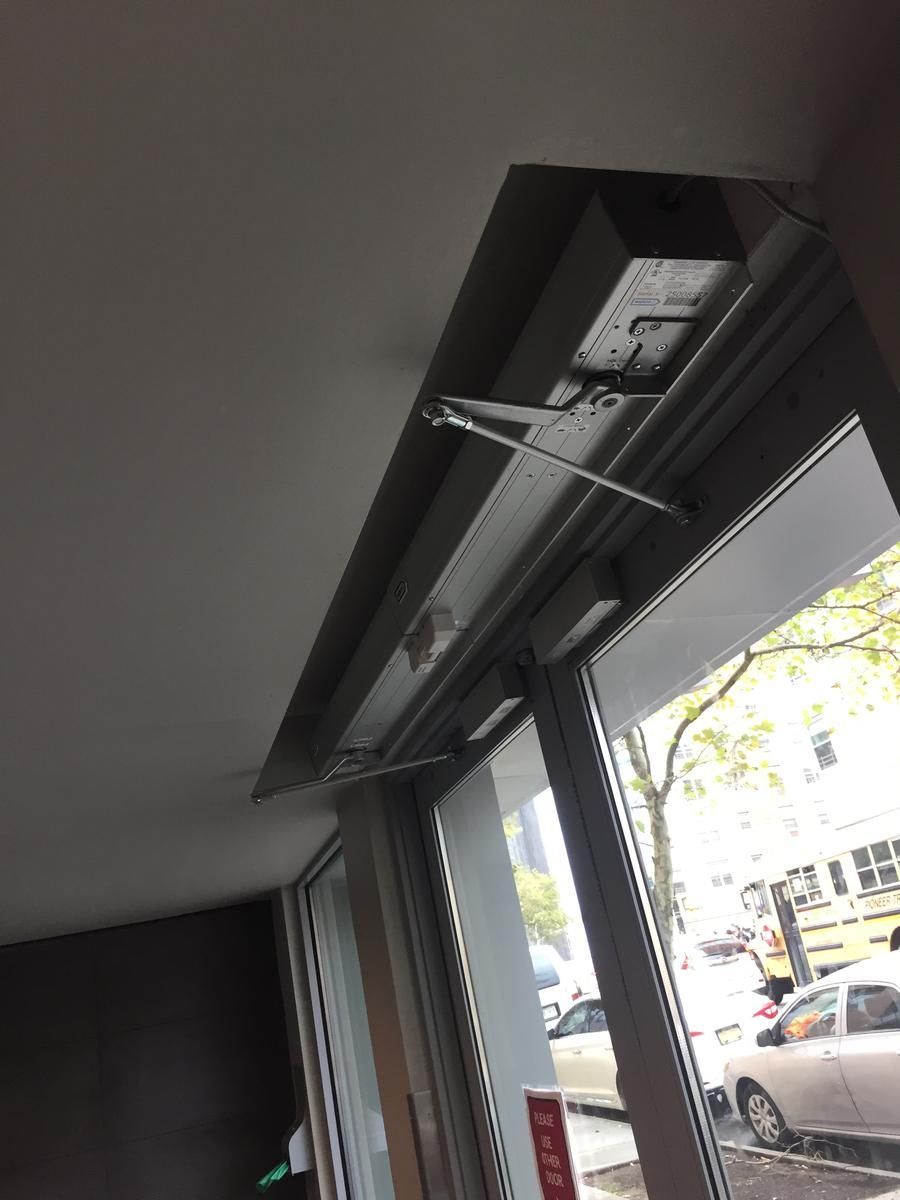 ADA automatic door operator mounted above an aluminum storefront entrance with exit hardware in the Bronx