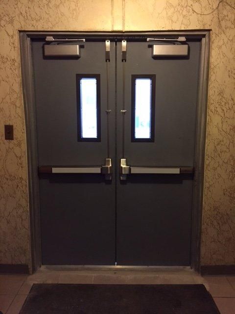 Pair of steel church doors with vertical rod panic exit devices and closers under an exit sign in the Bronx