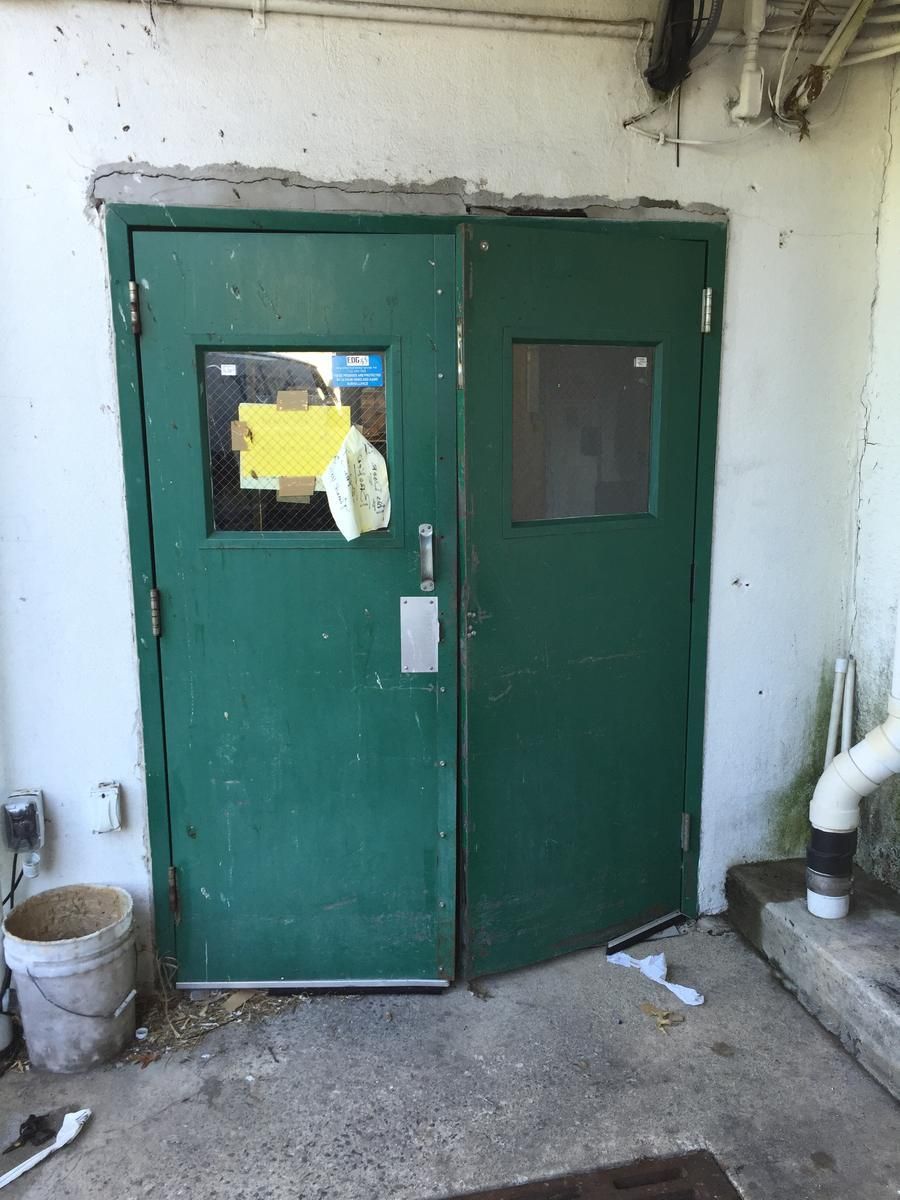 Worn green double doors with old hardware at a supermarket service entrance before replacement