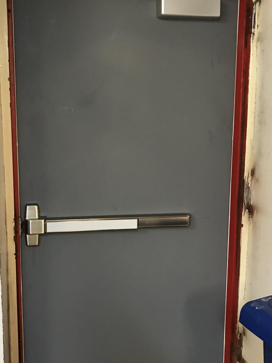 Close-up of a rim panic exit device and closer on a gray hollow metal door in Harlem