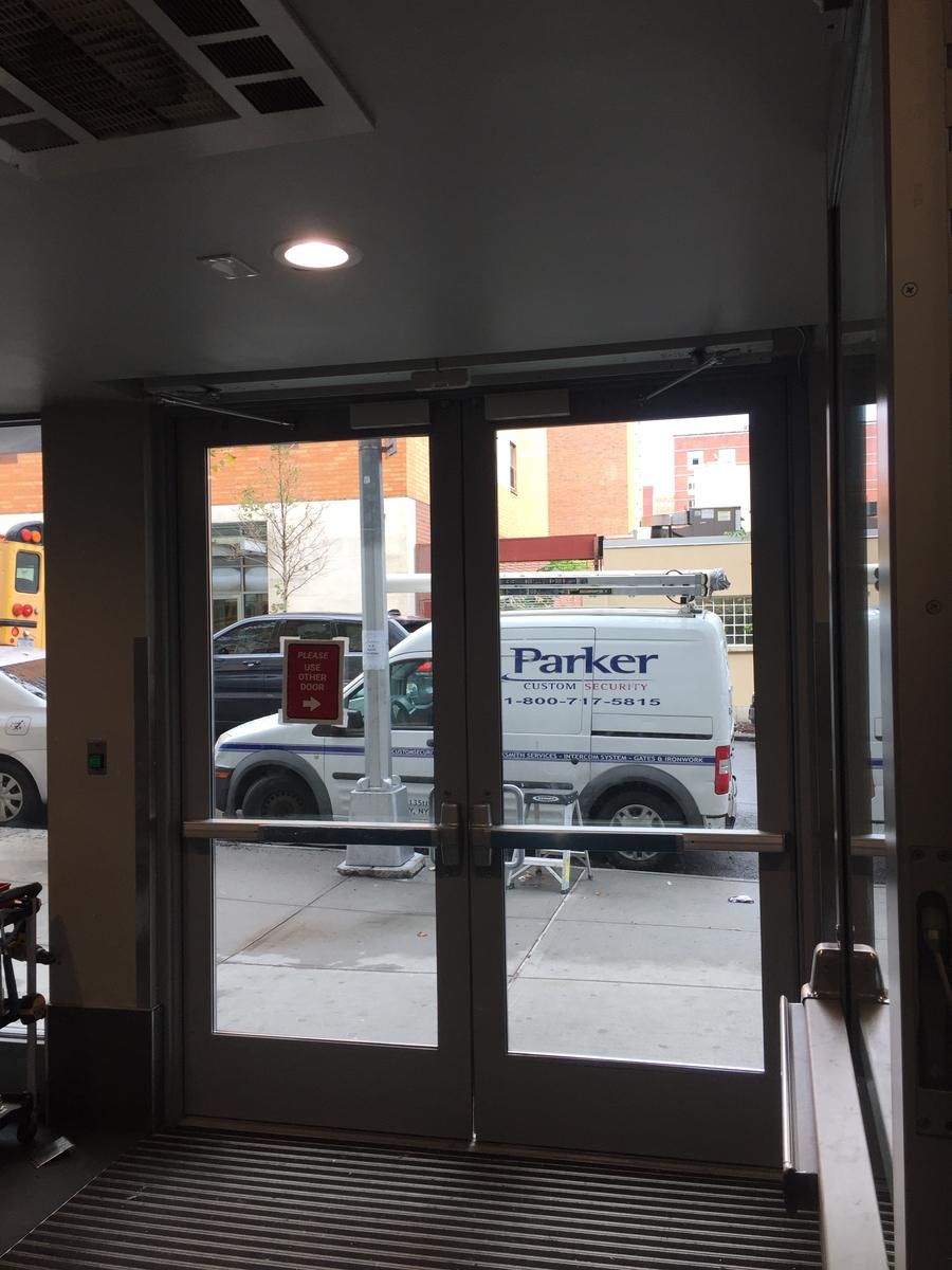 Aluminum storefront entrance doors with push-rail exit devices in the Bronx, with a Parker Custom Security van outside