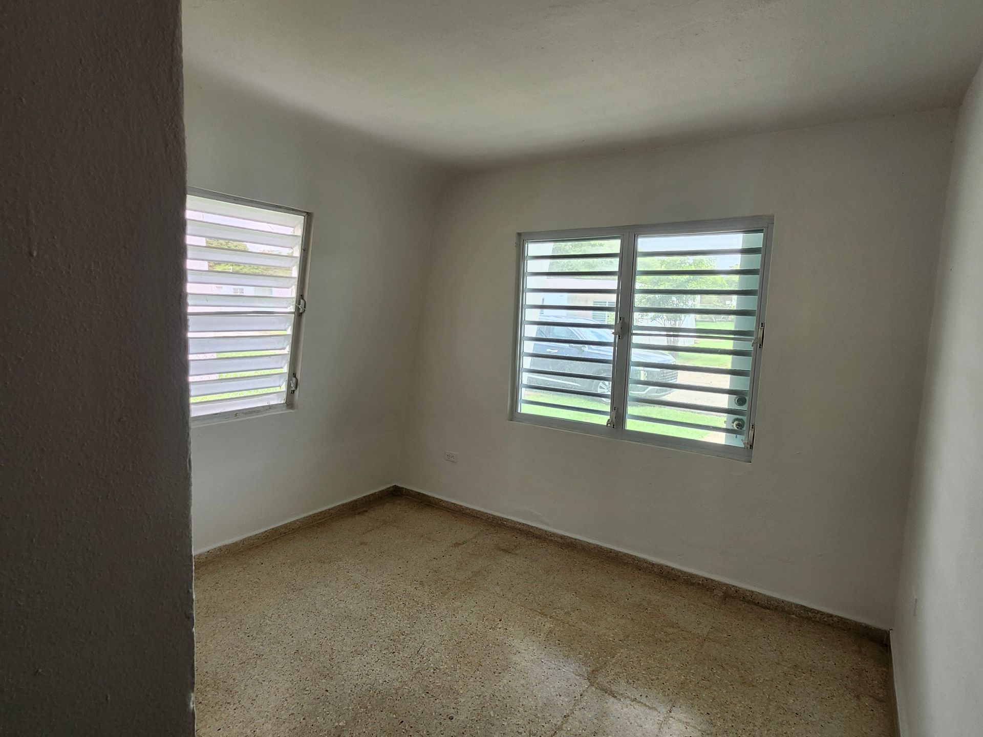 Empty white room with tiled floor and barred windows letting in daylight