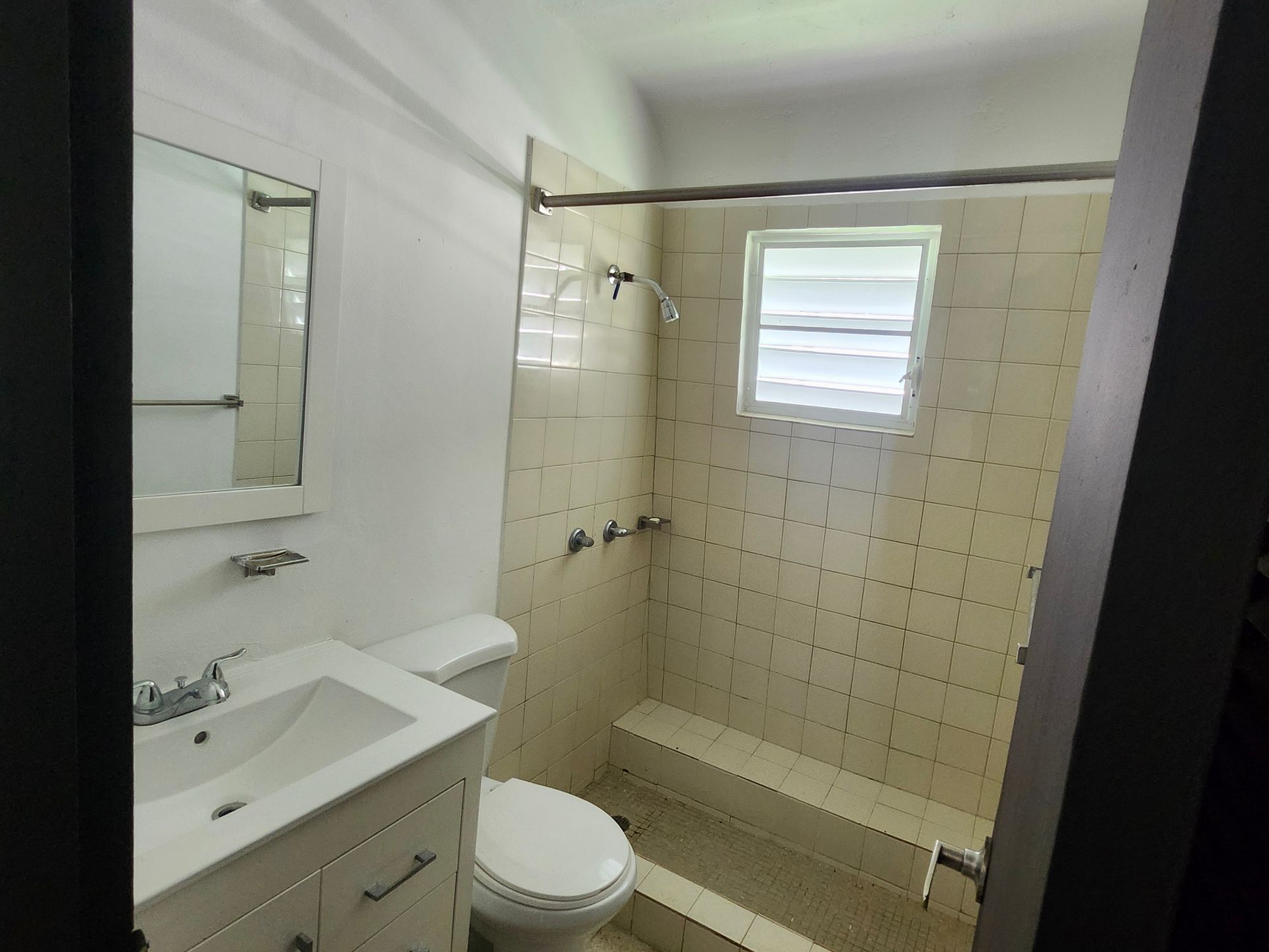 Small white bathroom with sink, toilet, mirror, and tiled shower-tub combo.
