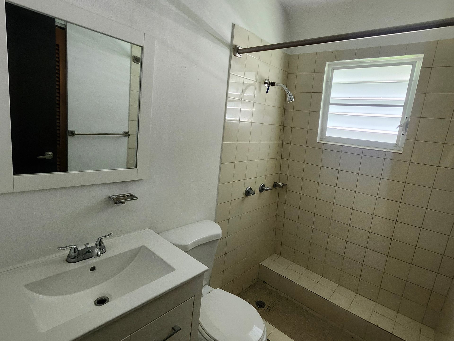 Small white bathroom with sink, toilet, shower, and a window with blinds