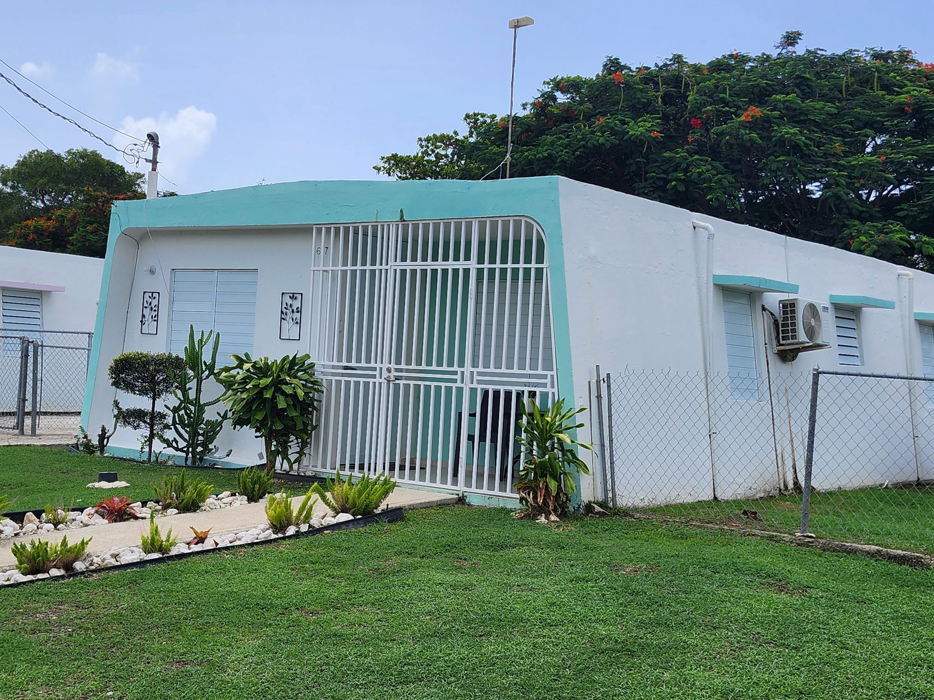 Small white building with turquoise trim, barred gate, and a grassy front yard under a cloudy sky