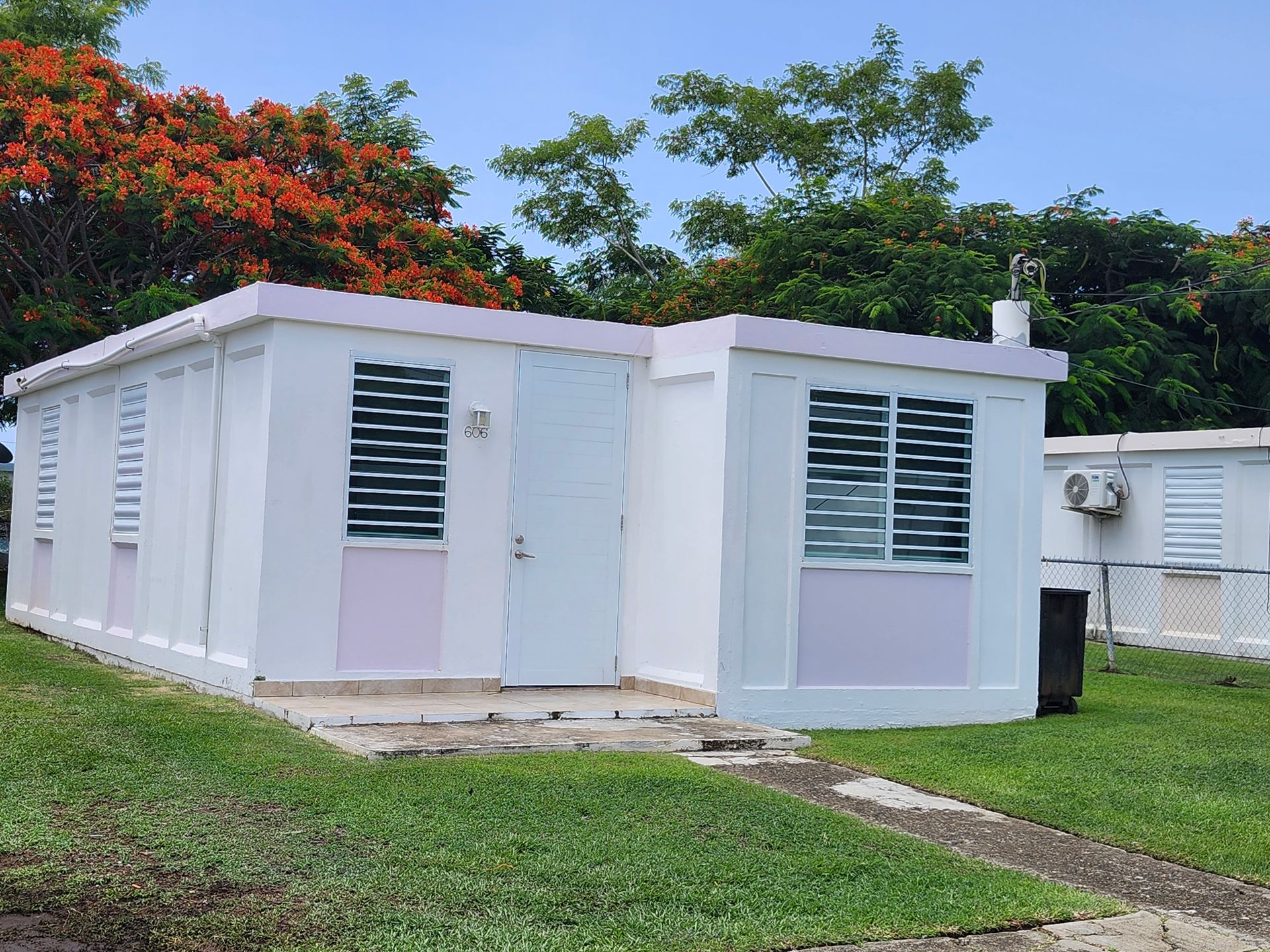Small white house with shutters and a grassy yard, set against trees and blue sky.