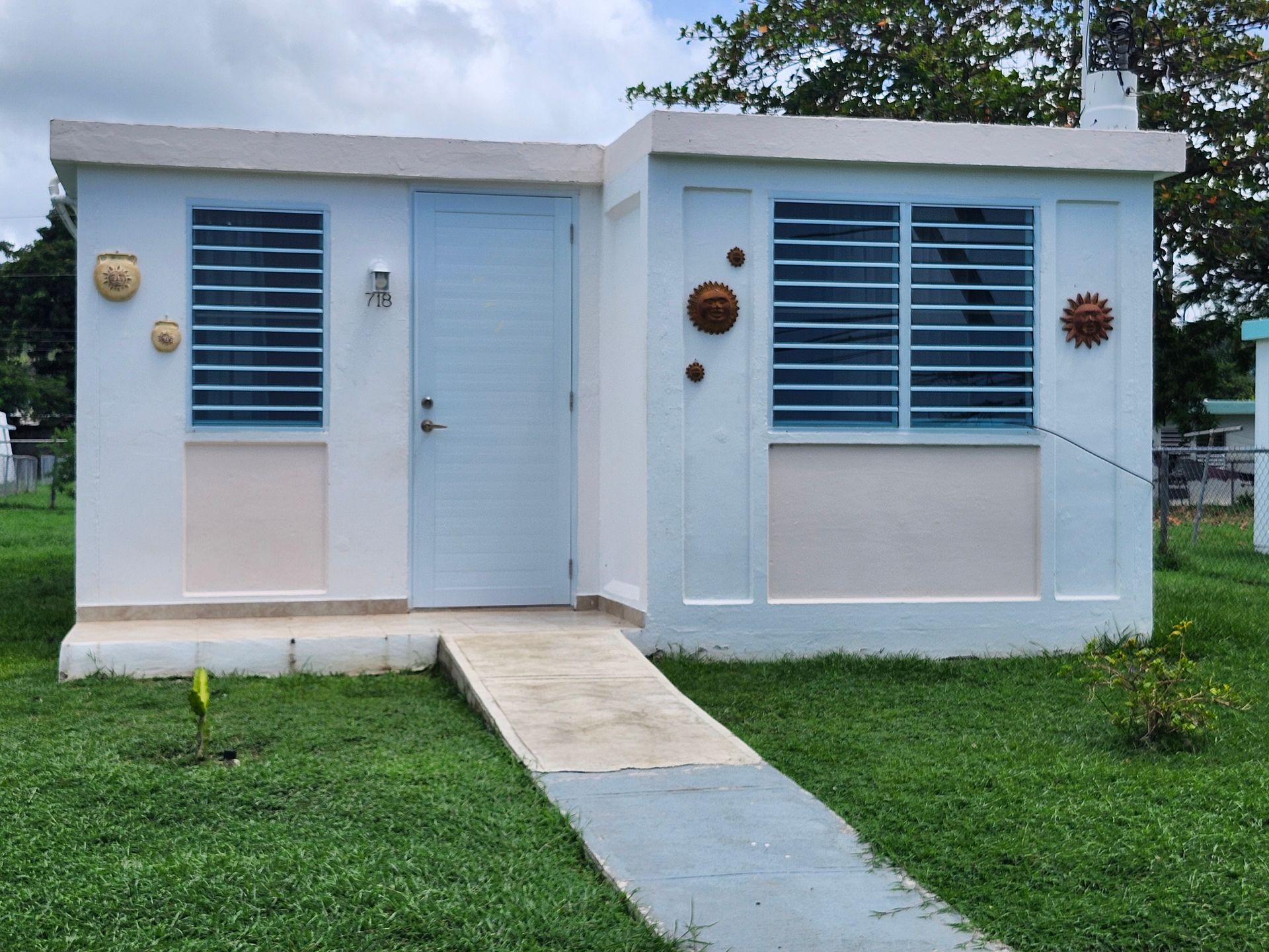 Small white house with blue door and windows, front porch ramp, and grassy yard