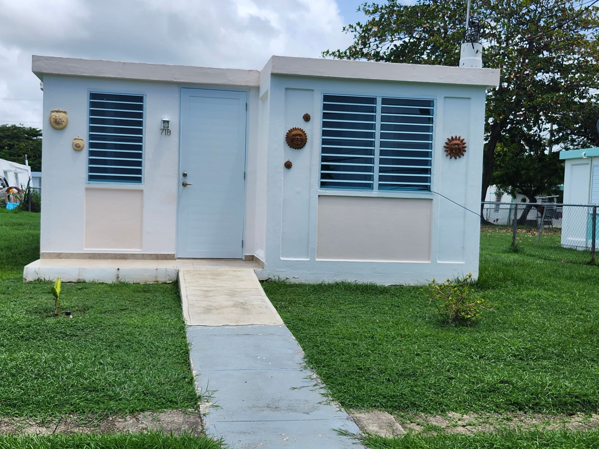 Small white building with blue shutters, centered walkway, and grassy yard under trees.