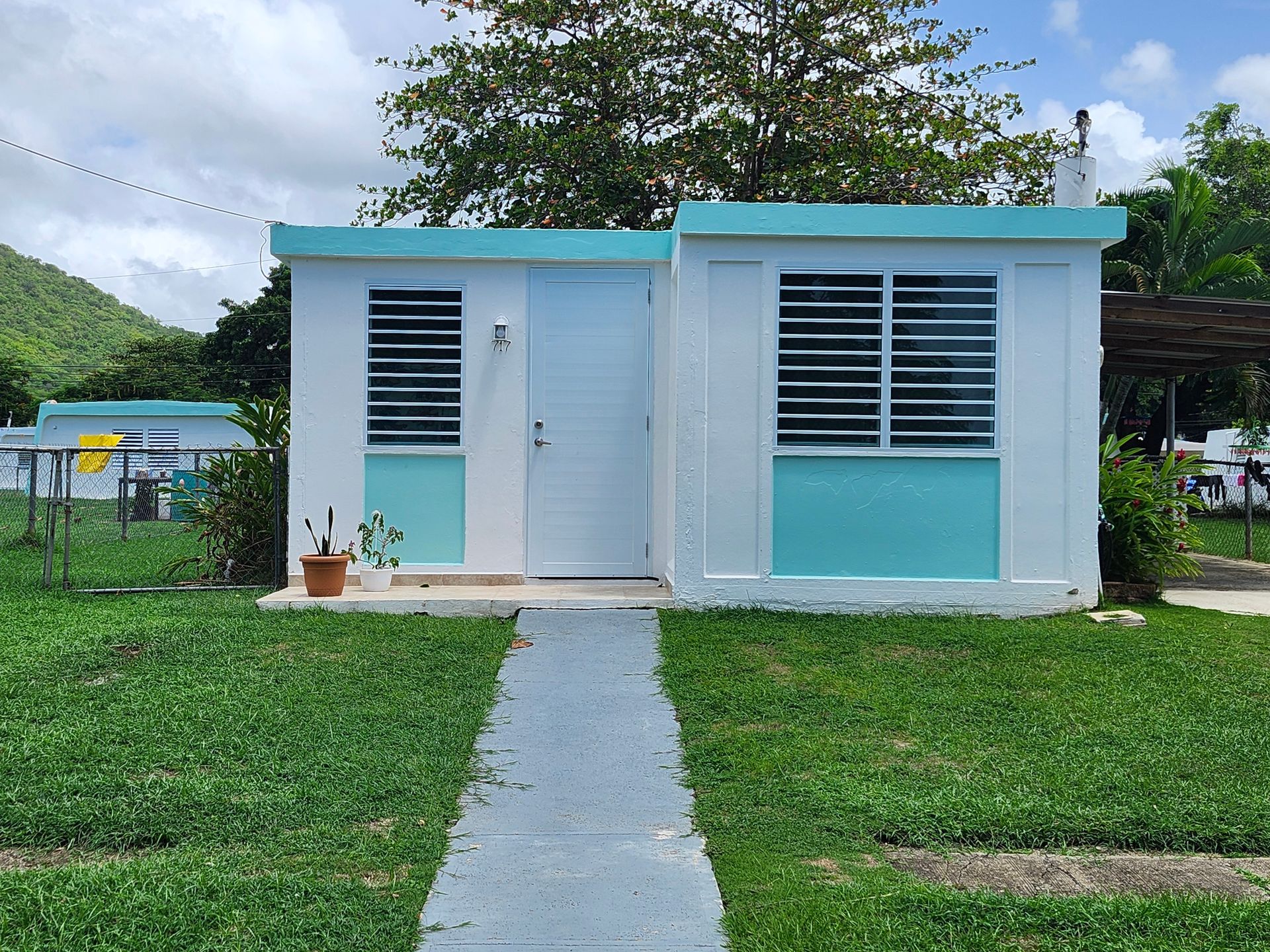 Small light-blue house with white trim and a front walkway, surrounded by a grassy yard