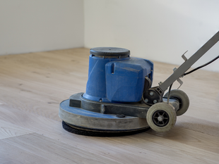 Blue floor buffer on a hardwood floor, with a person’s hands holding the handle.