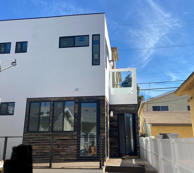 Modern white two-story house with black-framed windows, balcony, and a narrow side walkway on a sunny day