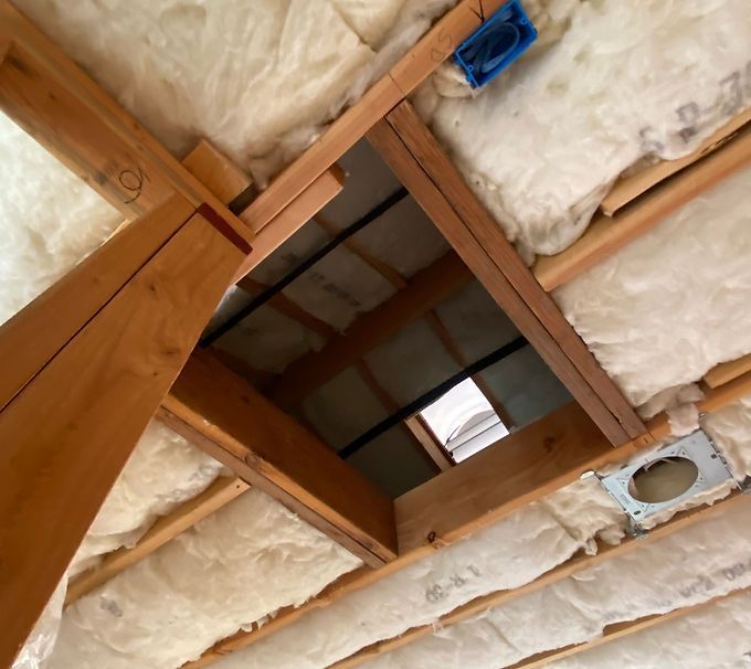 Ceiling framing with exposed insulation, wooden beams, a square opening, and a blue electrical box.