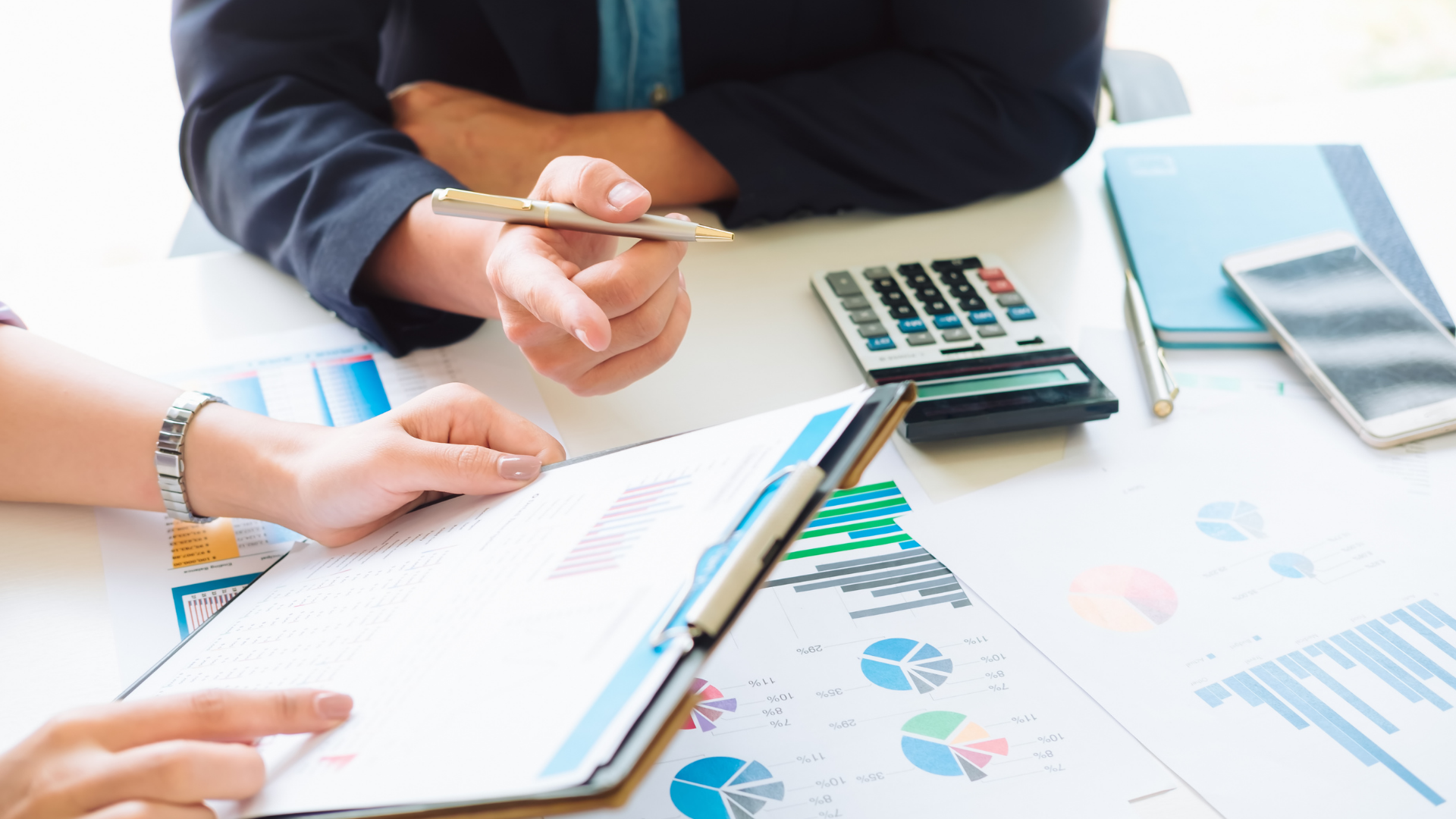 Hands pointing at colorful business charts and graphs on a tablet during a meeting