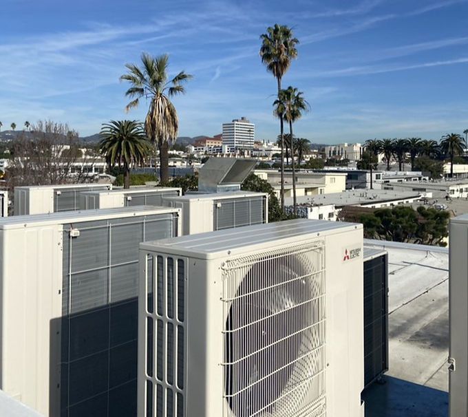 Rooftop HVAC units overlooking palm trees and a distant building under a clear blue sky.